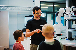 Mann erklärt Kindern etwas an einer Maschine.