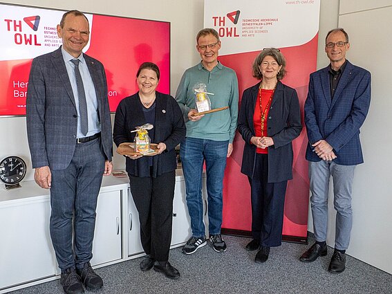 Foto: Fünf Personen posieren für ein Foto. Zwei halten ein Präsent in ihren Händen.