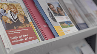 Broschüren des Familienservice zum Thema Kind und Beruf auf einem Regal.