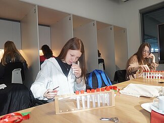 Zwei Mädchen haben Geruchsproben vor sich auf dem Tisch stehen. Eine der beiden riecht gerade daran.