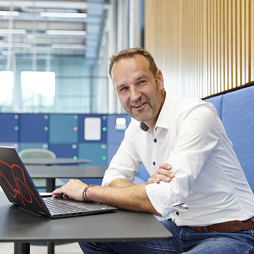 Prof. Dr. Paa sitzt mit einem Laptop an einem Cafeteriatisch und schaut in die Kamera.