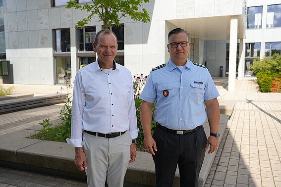 Foto: Zwei Männer, der Herr rechts im Bild in Uniform, stehen auf dem Innovation Campus in Lemgo. In Hintergrund ist das Gebäude InnovationSPIN zu sehen. 