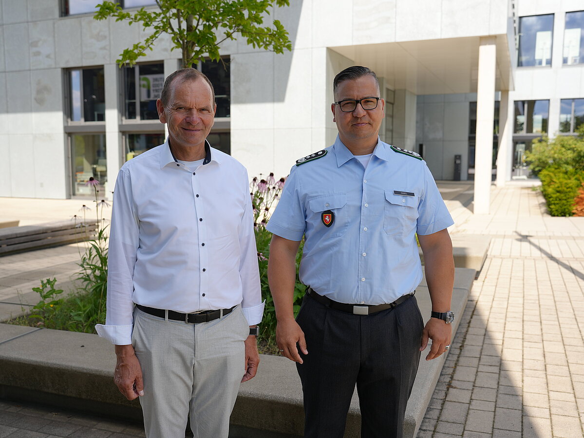 Foto: Zwei Männer, der Herr rechts im Bild in Uniform, stehen auf dem Innovation Campus in Lemgo. In Hintergrund ist das Gebäude InnovationSPIN zu sehen. 