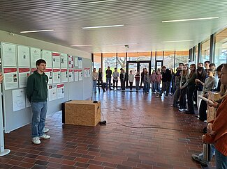 Viele Mädchen stehen in einem großen Raum und hören zu. Ein Mann hält einen Vortrag.