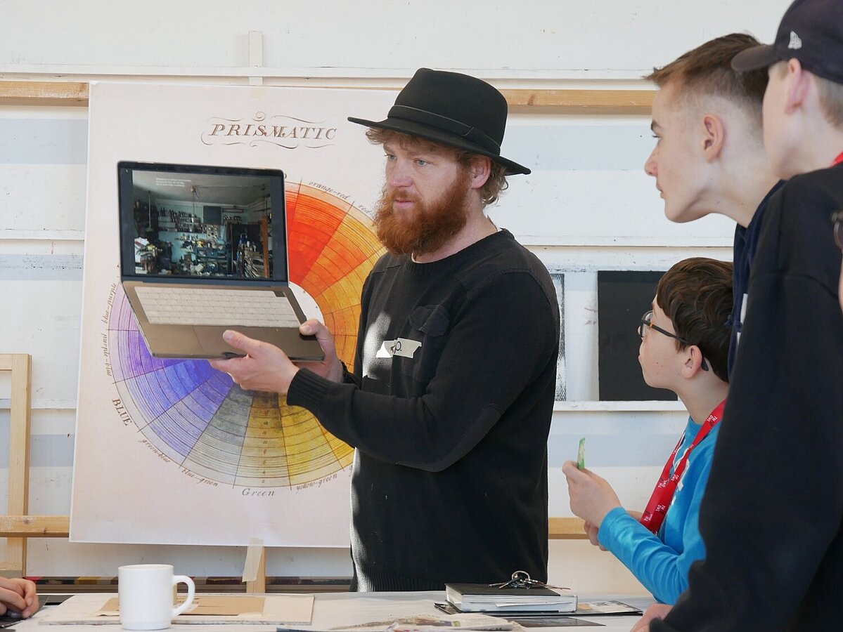 Ein Mann zeigt auf seinem Laptop verschiedene Kunstwerke. 