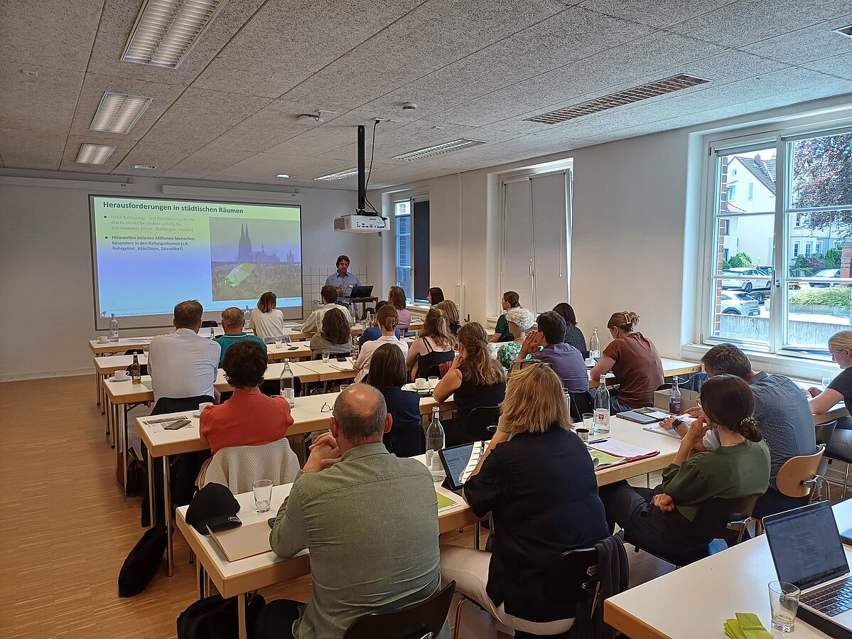 Tagungsteilnehmer:innen in einem Seminarraum. Von hinten zu sehen.