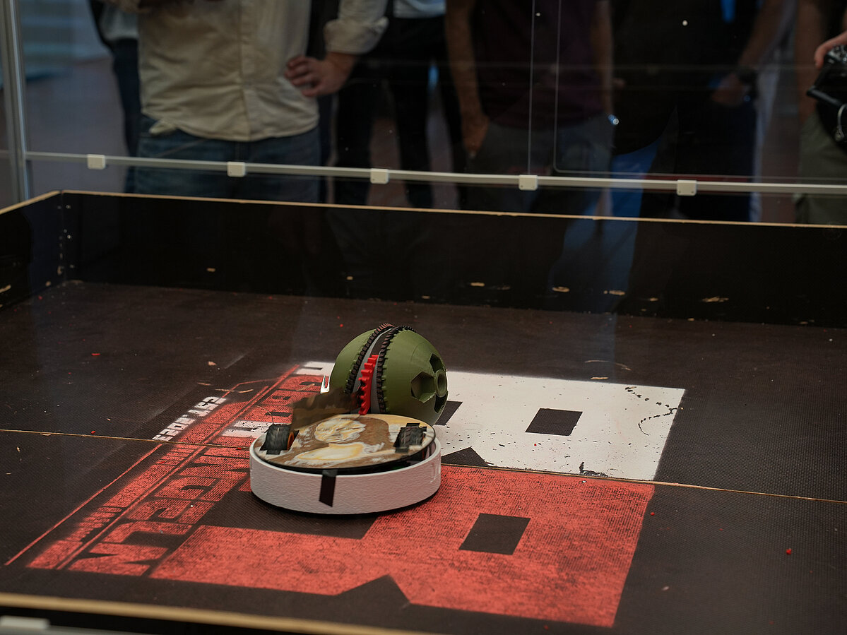 Zwei Roboter treten in der Arena gegeneinander an: "Runkugel" und "Mona Lisa" sind auf der Wettkampffläche in Aktion zu sehen. Die Plexiglasscheibe dahinter sorgt für die Sicherheit des Publikums.