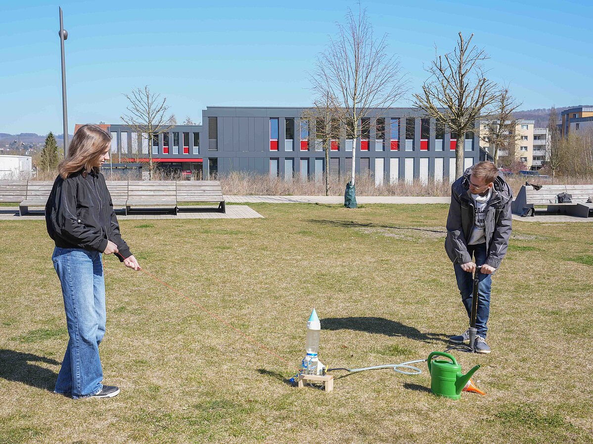 Ein Mädchen möchte ihre Wasserrakete starten lassen. Sie hält das Seil, ein erzeugt Druck in der Flasche, indem er dort Wasser reinpumpt.