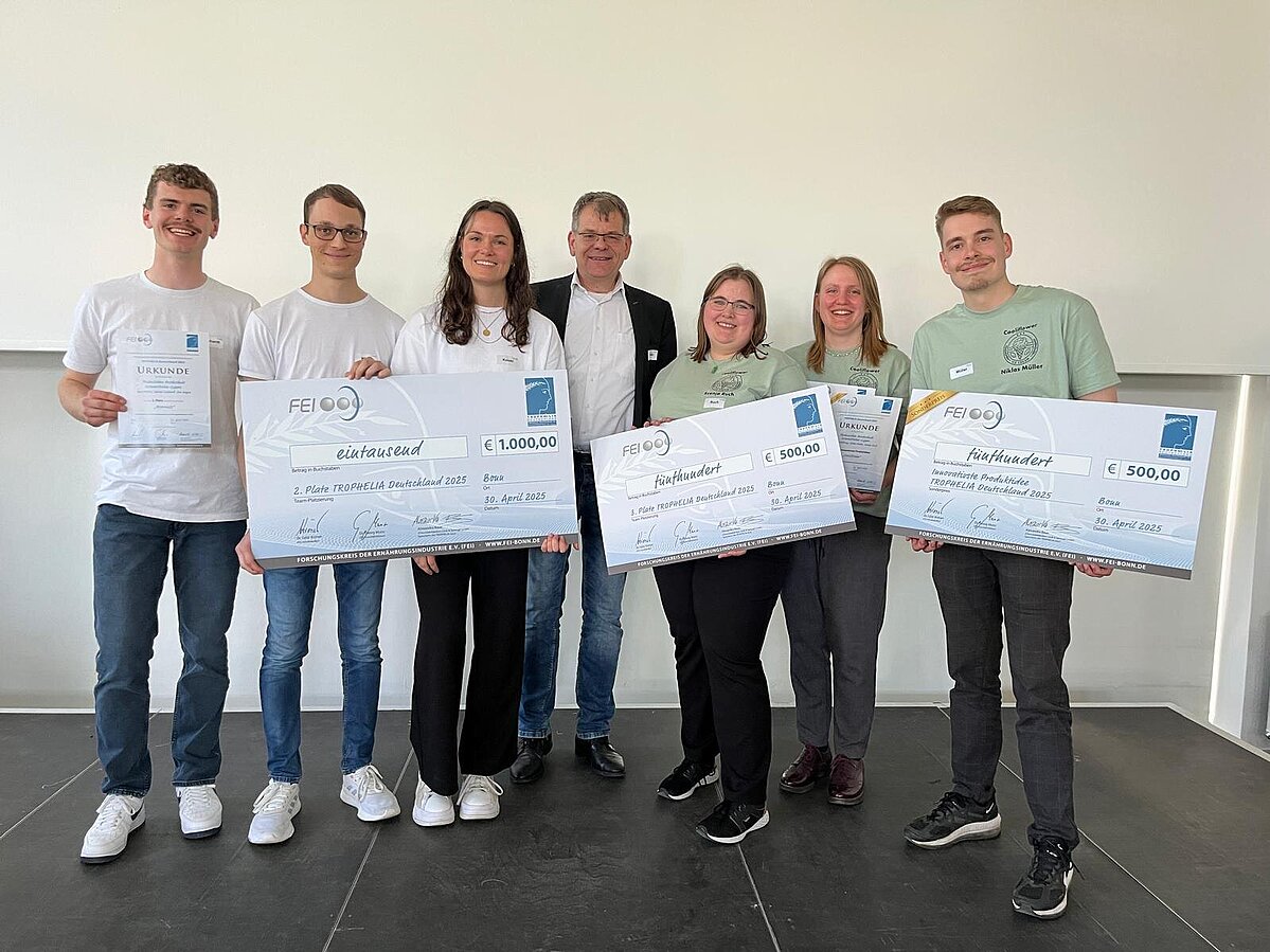 Eine Gruppe von Studierenden und ein Professor mit großen Tafeln auf denen ihre Preise zu sehen sind.