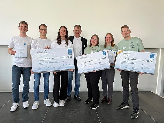 Eine Gruppe von Studierenden und ein Professor mit großen Tafeln auf denen ihre Preise zu sehen sind.