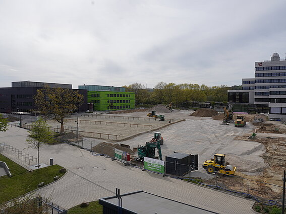 Foto: Blick auf den neuangelegten Schotterparkplatz zwischen Bunsenstraße und Campusalle. Hintergrund stehen moderne Laborgebäude. 