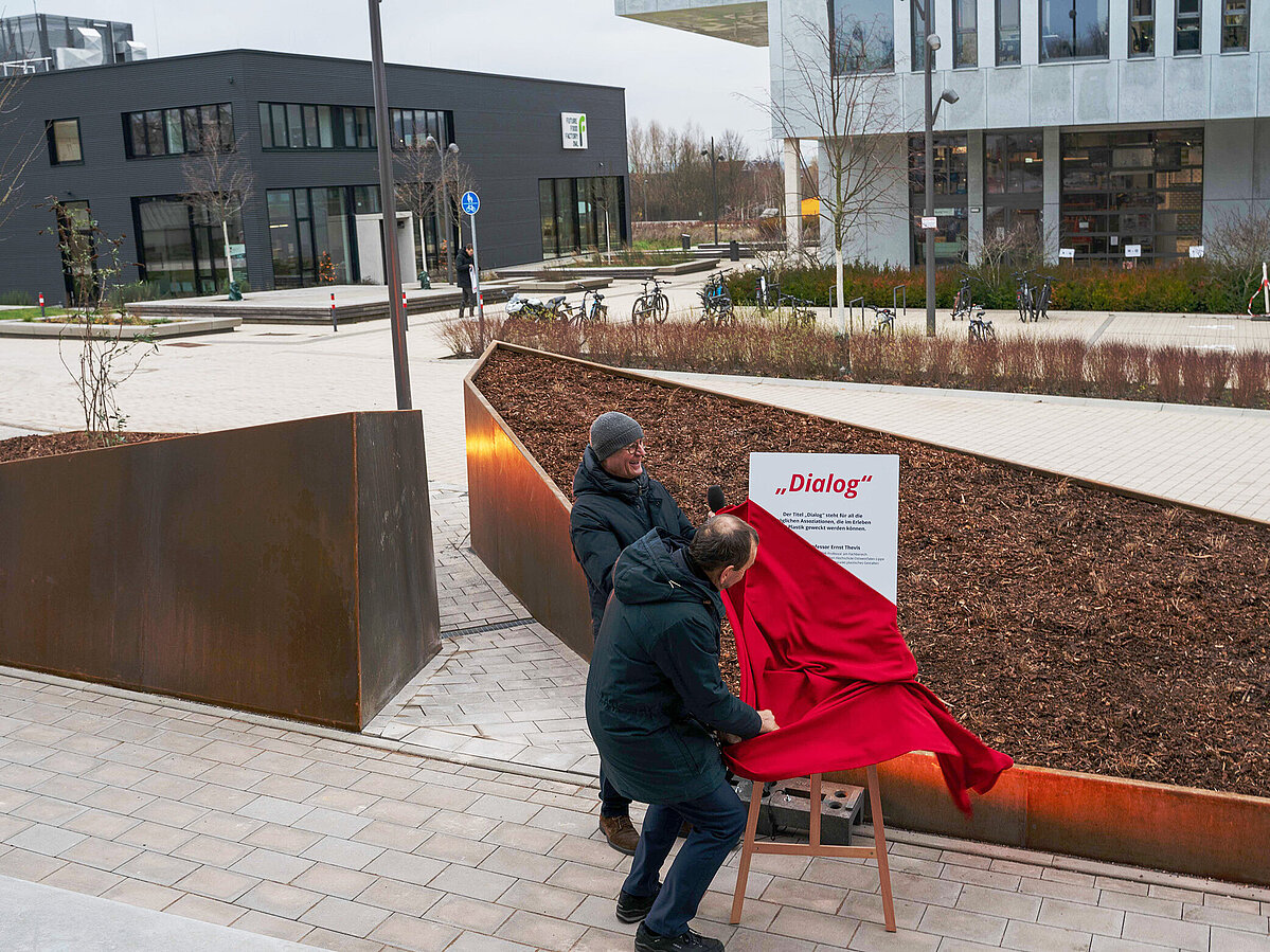 Zwei Männer enthüllen ein Schild mit der Aufschrift "Dialog"