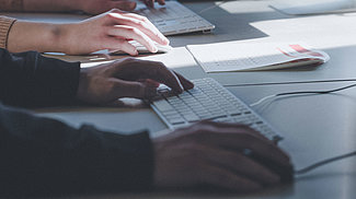 Zu sehen sind die Hände einer Person, von denen eine an einer Tastatur arbeitet und die andere eine Computermaus festhält