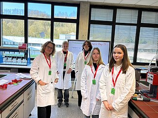 Vier Mädchen und eine Frau posieren in Laborkitteln für ein Foto. 