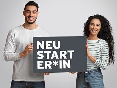 Zwei Personen halten ein Schild hoch, auf dem Neustarter:in steht.