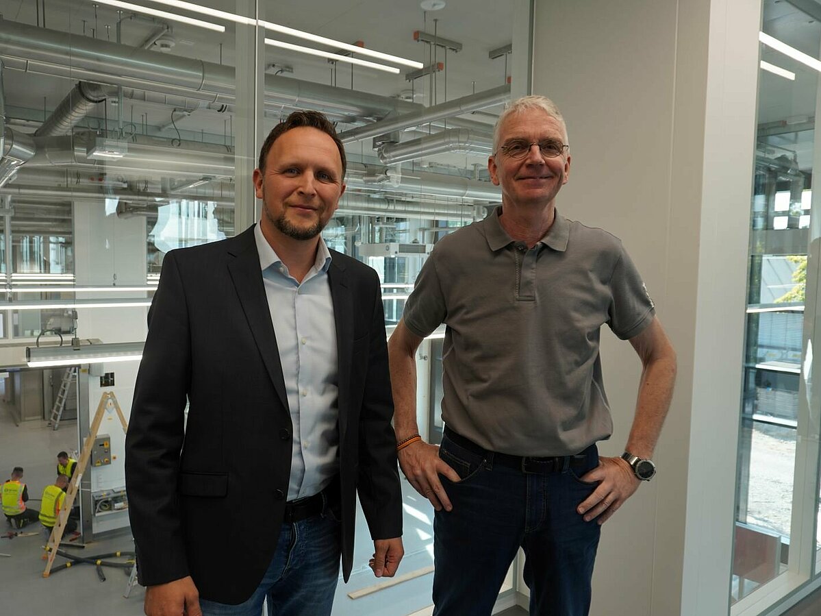Zwei Männer vor Fensterscheibe mit Blick in Laborhalle