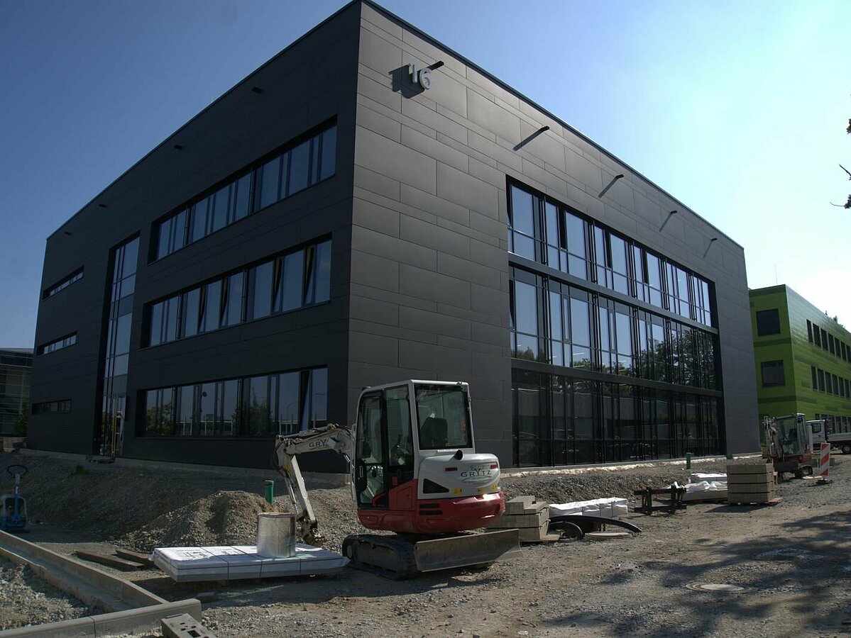 Neuer, dreigeschossiger, dunkelgrauer Flachdachbau. Außenanlagen noch im Bau.