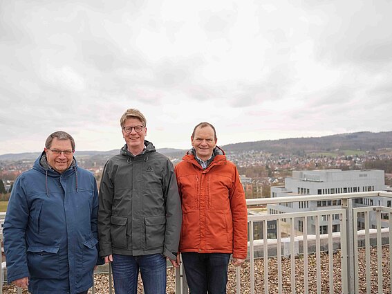 Foto: Drei Männer stehen an einem Geländer einer Dachterasse und werden fotografiert.