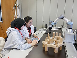 Zwei Mädchen beobachten einen Roboter.