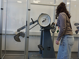 Ein Mädchen steht vor dem Kerbschlagbiegeversuch und legt ein kaltes Stahlstück hinein. 