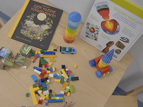Spielzeug auf einem Tisch Bücher, Spielfiguren und Klötze liegen auf einem Holztisch in einem Eltern-Kind-Raum der TH OWL