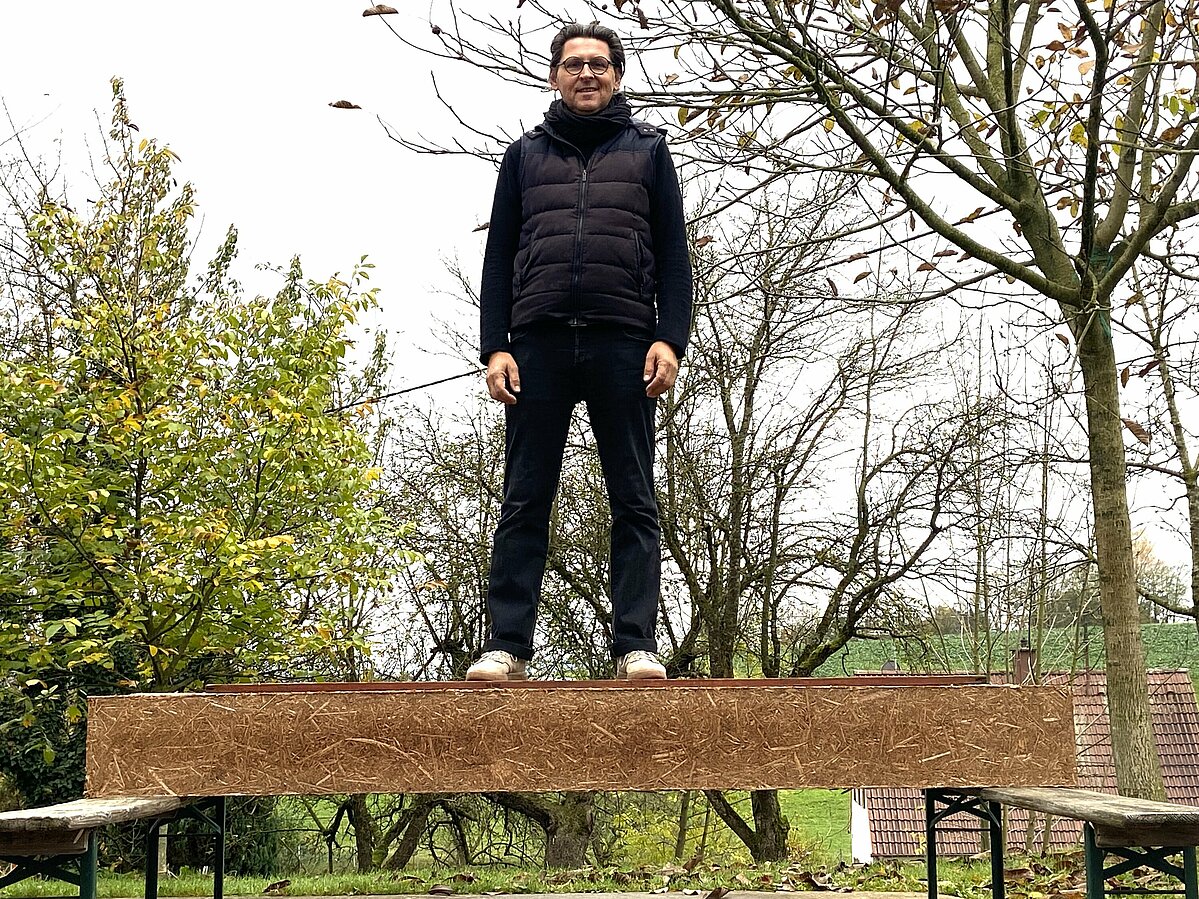 Professor Lux steht auf einem Balen aus Rohrkolben, der an den Enden auf Bierbänken liegt. 