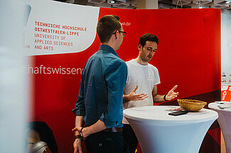 Junger Mann berät andern jungen Mann am Messestand.