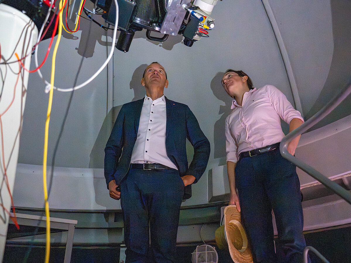 A man and a woman are standing in front of a telescope.