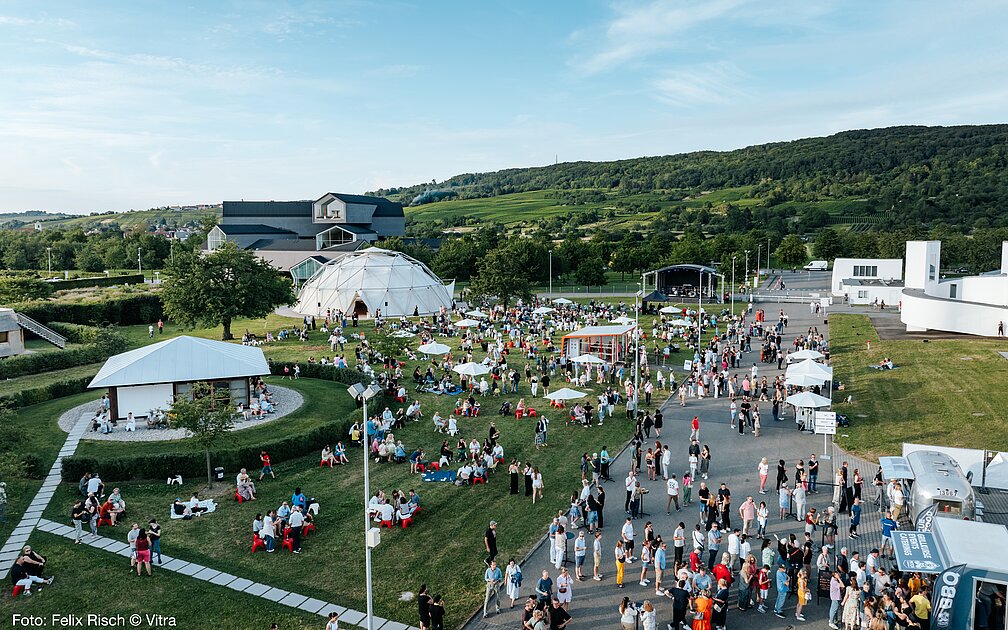 Luftaufnahme des Vitra Campus in Weil am Rhein mit vielen Menschen und Aktivitäten an Pavillons zwischen Vitra Design Museum und Vitra Haus