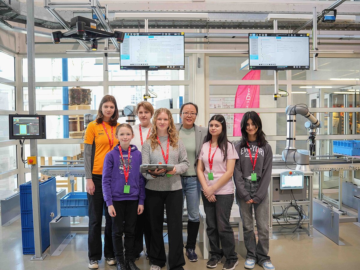 Mehrere Mädchen posieren für ein Gruppenfoto vor einem Roboter. 