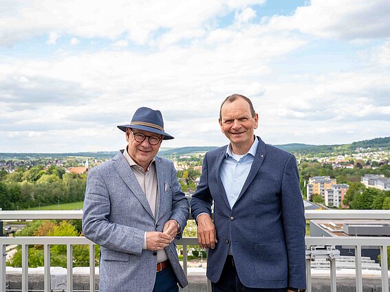Foto: Zwei Männer stehen auf einer Dachterasse und machen ein Foto.