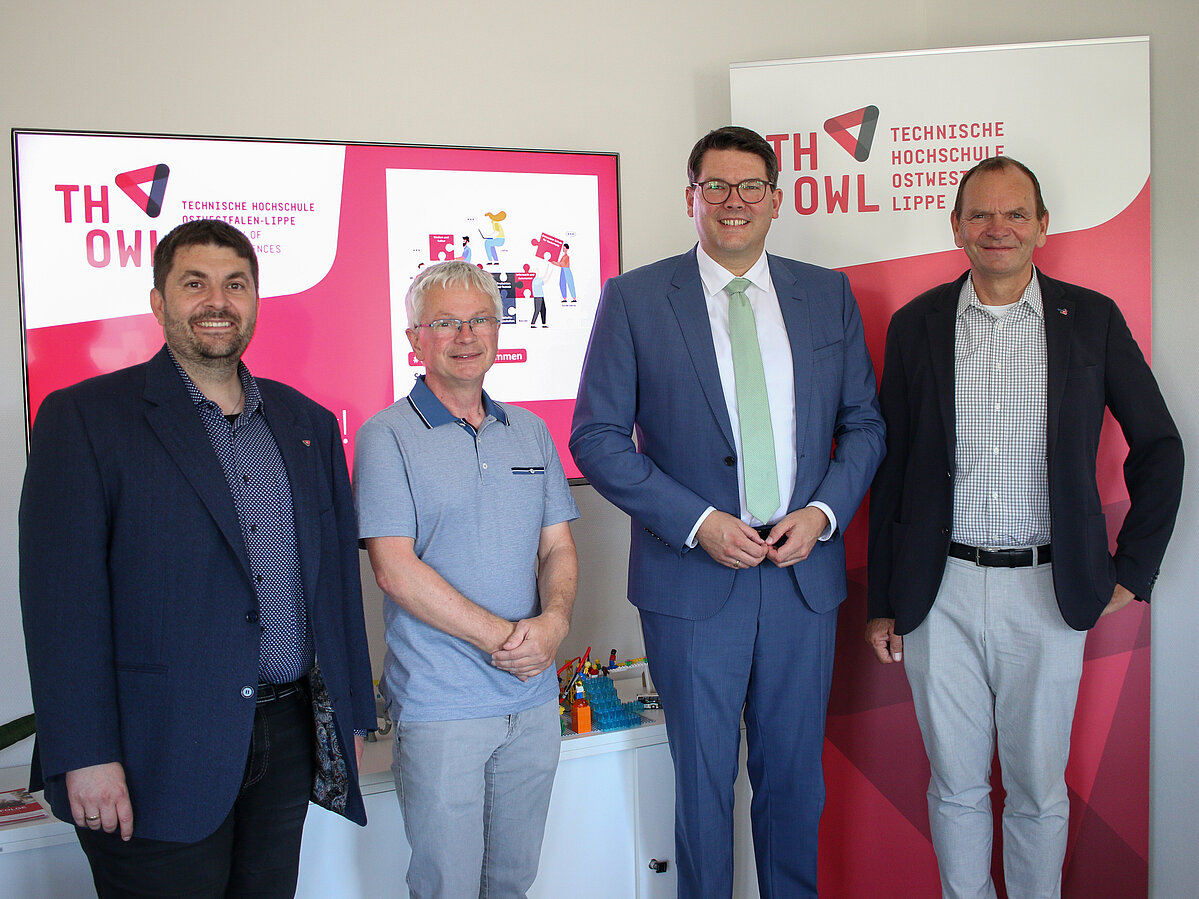 Gamecraft vorgestellt (v. r.): TH-OWL-Präsident Professor Dr. Jürgen Krahl, Bundestagsabgeordneter Joachim Ebmeyer, Professor Dr. Guido Falkemeier und Professor Dr. Josel Löffl stehen nebeneinander in einem Raum. Dahinter befindet sich ein Monitor und ein Plakat der TH OWL..
