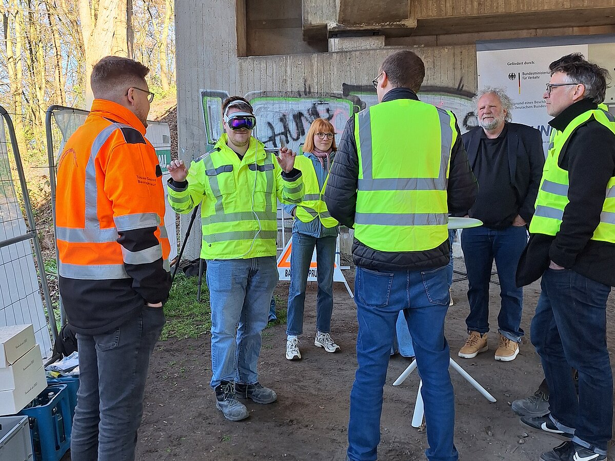 Gruppe von Menschen unter einer Betonbrücke, analysieren diese mit Hilfe von VR-Brillen