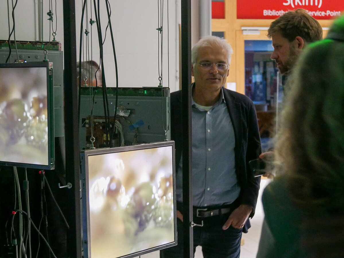 Besucher der Ausstellung stehen neben offengelegten Displays
