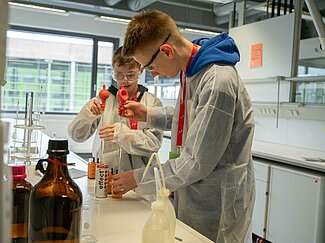 Zwei Jungen mit Kitteln arbeiten im Chemielabor.