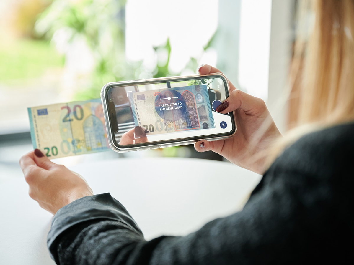 Junge Frau überprüft mit einer App die Echtheit einer Banknote