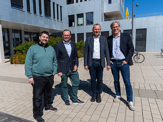 Photo: Four men are standing side by side, looking at the camera. In the background is the InnovationSPIN on the Lemgo campus. 