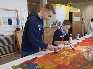 Zwei Jungen malen mit einem Pinsel ein Kunstwerk.