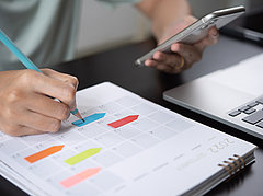 eine Hand notiert Termine im Kalender, die andere scrollt am Smartphone