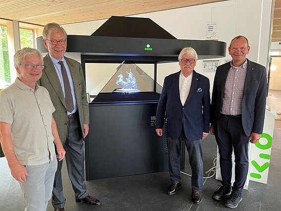 Photo: Four men at KIO; a 3D projection is visible in the center of the background.