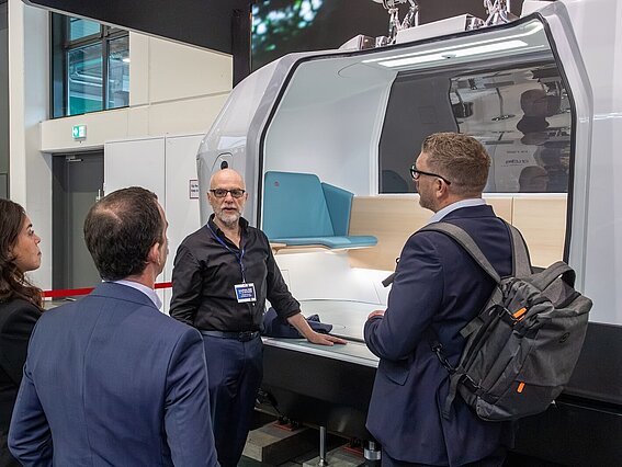 Foto: Drei Männer und eine Frau stehen an einem Messestand zu dem Thema MONOCAB.