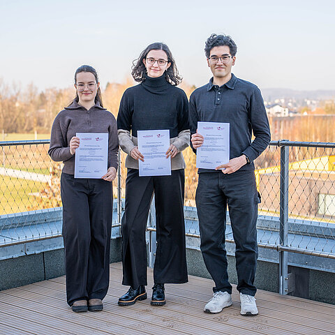 Foto: Zwei Stipendiatinnen und ein Stipendiat der TH OWL stehen nebeneinander auf einer Terasse des InnovationSPIN in Lemgo und halten ihre Urkunden. 