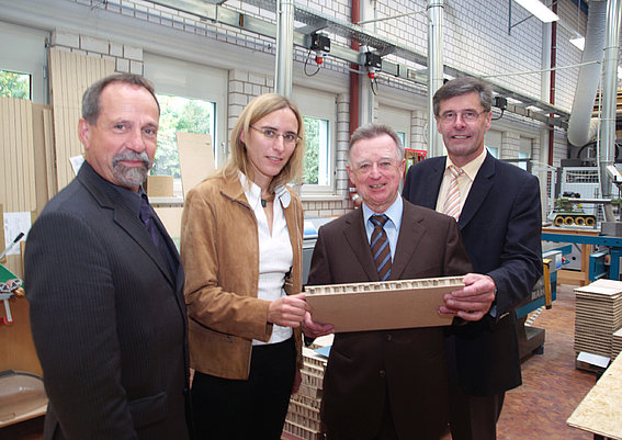Grafik: Ein Jahr Stiftungsprofessur Holzbauproduktion mit (v. l.) Rektor Prof. Tilmann Fischer, Prof.'in Katja Frühwald, Dr. Hannes Frank und Landrat Friedel Heuwinkel.