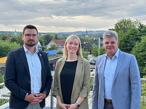 Foto: Drei Personen, zwei Männer und eine Frau in der Mitte, blicken in die Kamera.