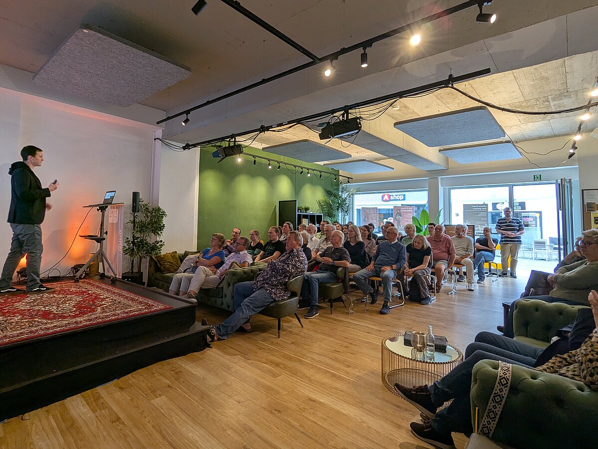 Photo: In the "anno 1578" event hall in downtown Lemgo, an audience sits and listens to a lecture. A man on the left side of the picture is standing on a podium.
