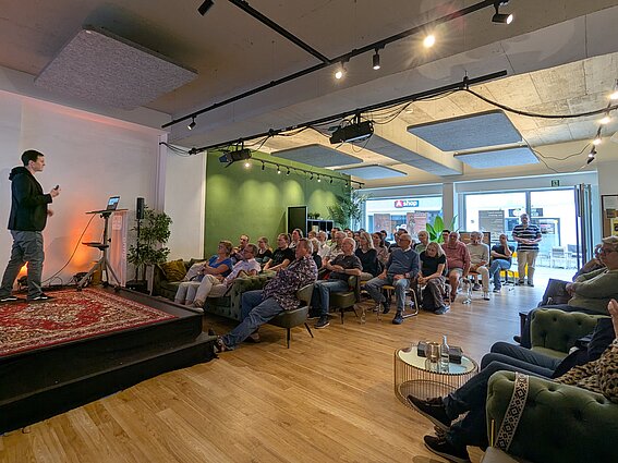 Photo: In the "anno 1578" event hall in downtown Lemgo, an audience sits and listens to a lecture. A man on the left side of the picture is standing on a podium.