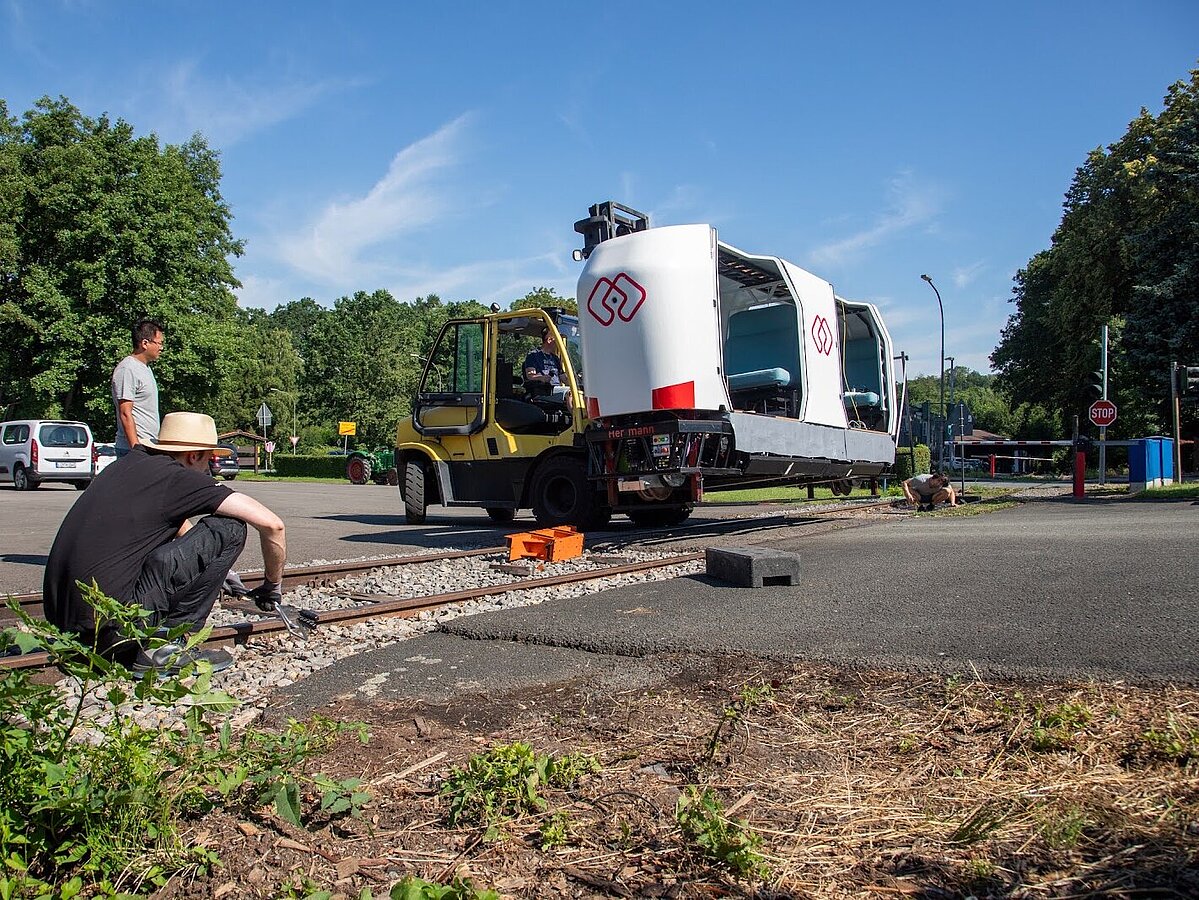 Foto: Das Versuchsfahrzeug MONOCAB wird von einem Gabelstapler auf die Schiene gesetzt. 