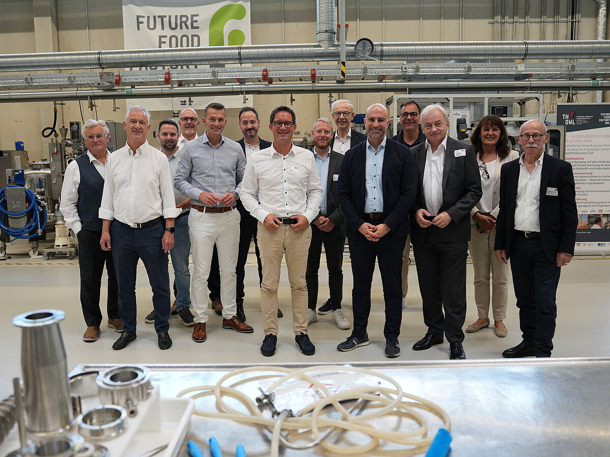 Die Delegation aus Hermagor und dem Kreis Minden-Lübbecke stehen zusammen in der Maschinenhalle der Future Food Factory OWL. Sie informierten sich dort über aktuelle Forschungs- und Transferprojekte.