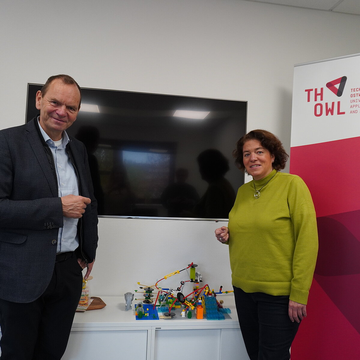 Foto: Ein Mann und eine Frau stehen in einer Gesprächssituation in einem Büro.