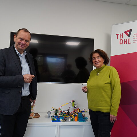 Foto: Ein Mann und eine Frau stehen in einer Gesprächssituation in einem Büro.